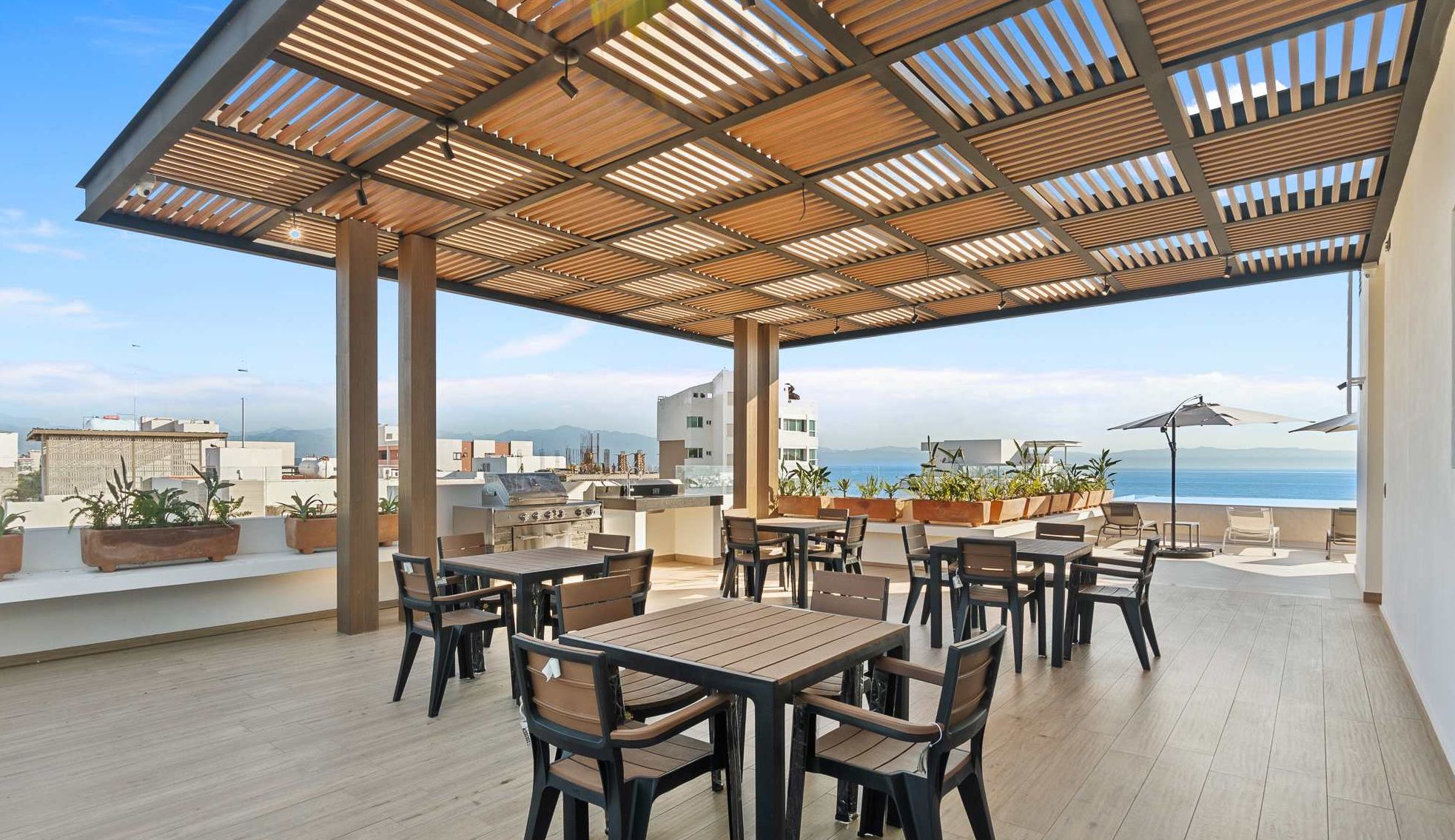 Un patio al aire libre con mesas y sillas de madera, una parrilla y plantas en macetas.