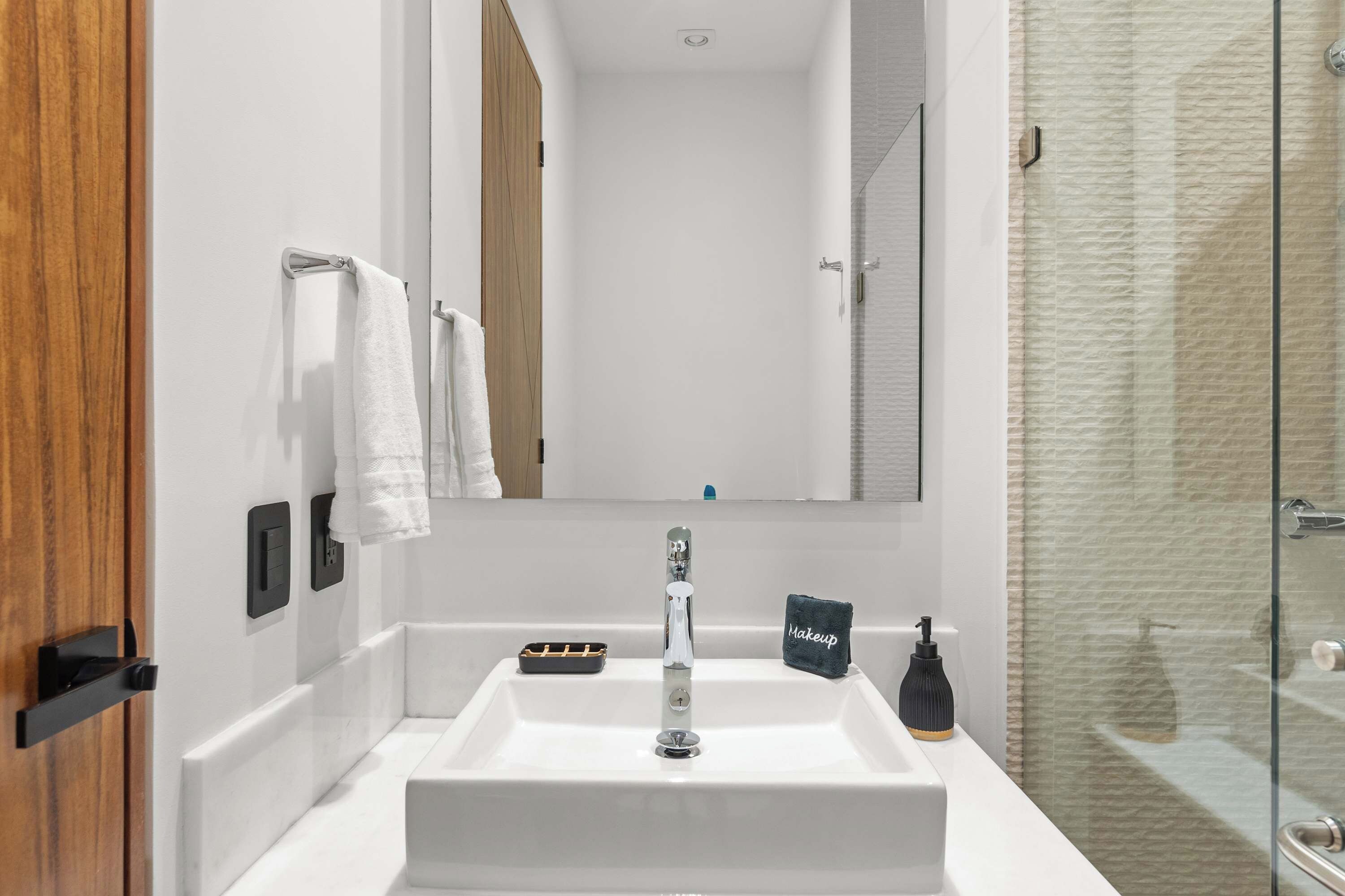 Un baño moderno con un lavabo blanco, un espejo y una cabina de ducha de vidrio.