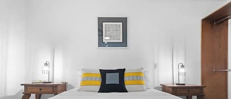 A bedroom with a bed, two bedside tables, a framed artwork on the wall, and a door.