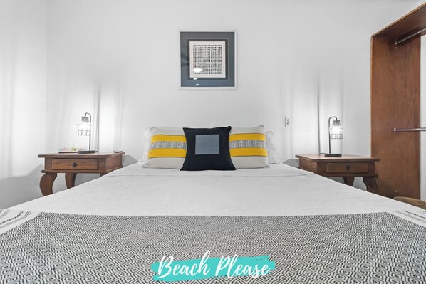 A bedroom with a bed, two bedside tables, a framed artwork on the wall, and a door.