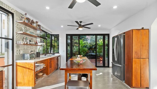 Une cuisine moderne avec un îlot central en bois, des étagères intégrées, un grand réfrigérateur et un ventilateur de plafond.