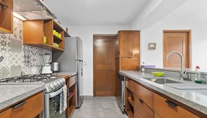 Une cuisine de taille réduite, équipée d’une cuisinière à gaz, d’un réfrigérateur et de meubles de rangement en bois.
