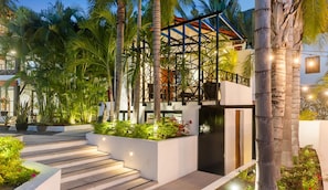 A modern building with a geometric facade, surrounded by lush greenery and palm trees.