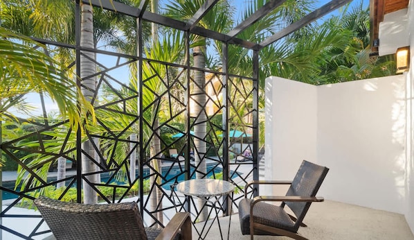 A covered outdoor seating area with a pool in the background, surrounded by palm trees.