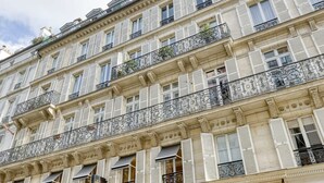 Un edifici de diverses plantes amb façanes blanques, múltiples balcons amb baranes de ferro forjat i persianes uniformes.
