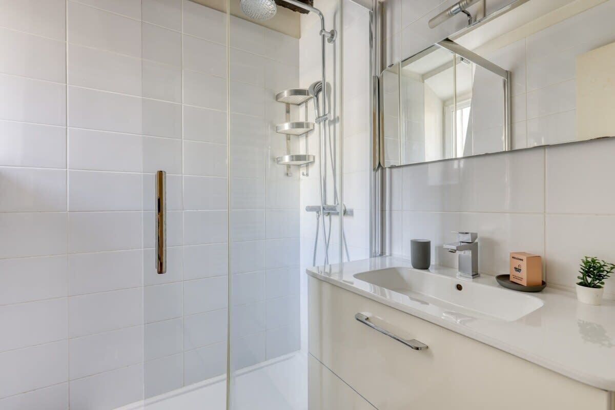 A modern bathroom with a glass-enclosed shower, a large mirror, a sink, and a small plant.