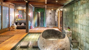 Ein Spa-Raum mit einer großen Steinbadewanne, Holzboden und einer gefliesten Wand.