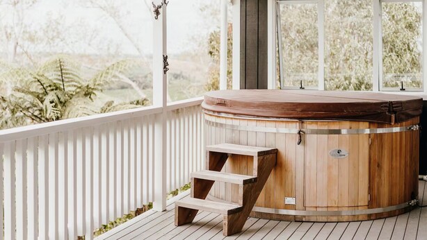 Een houten jacuzzi met een trap en een witte leuning, en een raam met uitzicht op bomen.