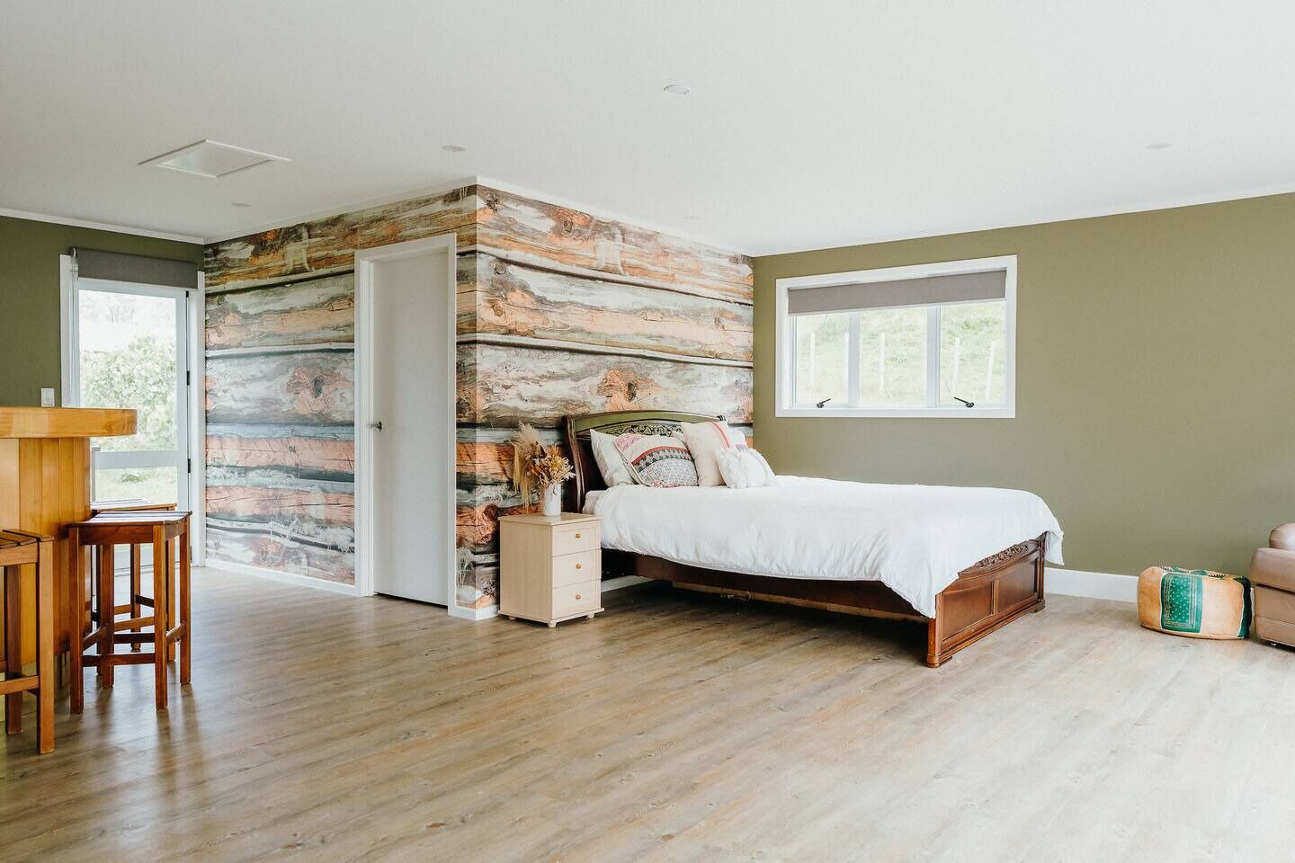 Une chambre à coucher avec un lit en bois, une table de chevet, un bureau en bois et une grande fenêtre.