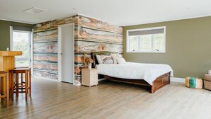 Een slaapkamer met een houten bed, een nachtkastje, een houten bureau en een groot raam.
