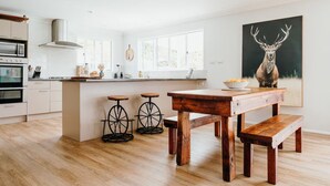 Een moderne keuken met een centraal eiland, houten krukken en een groot schilderij van een hert.