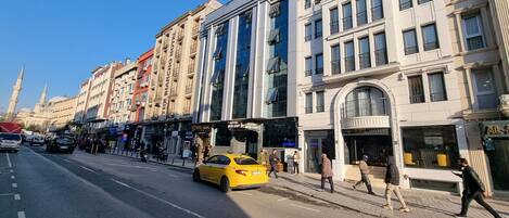 A street with a yellow taxi, buildings with shops, and a mosque in the background.