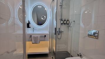 Een moderne badkamer met een douchecabine van glas, een ronde spiegel met verlichting, een toilet en een wastafel met een handdoekhouder.