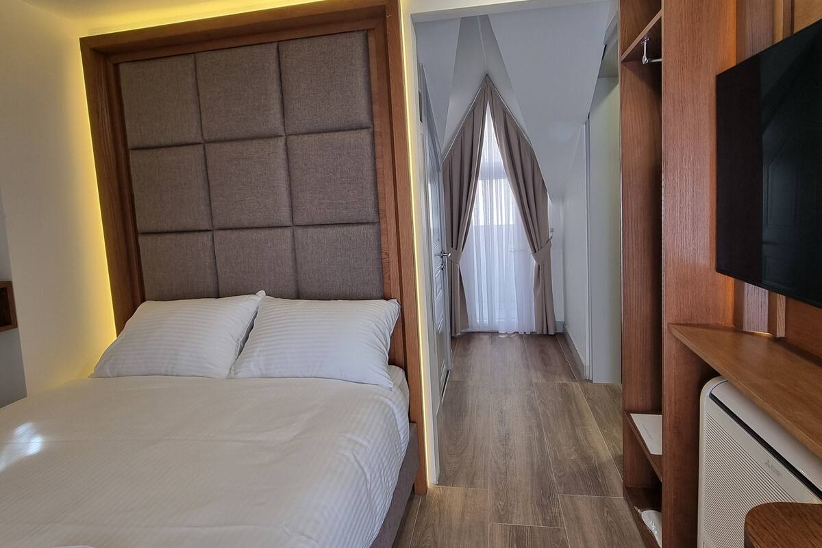 A hotel room with a large bed, a TV, and a wooden cabinet.