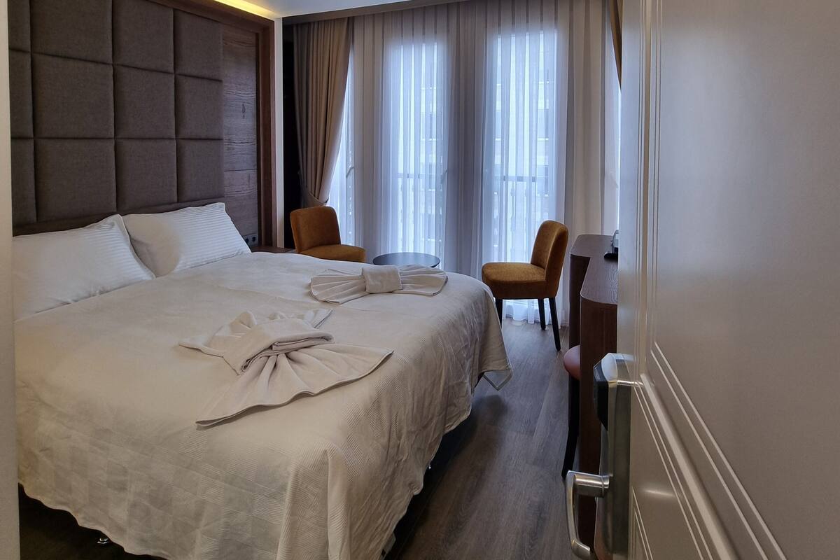 A hotel room with a large bed, a desk, two chairs, and a view of the outdoors through the window.