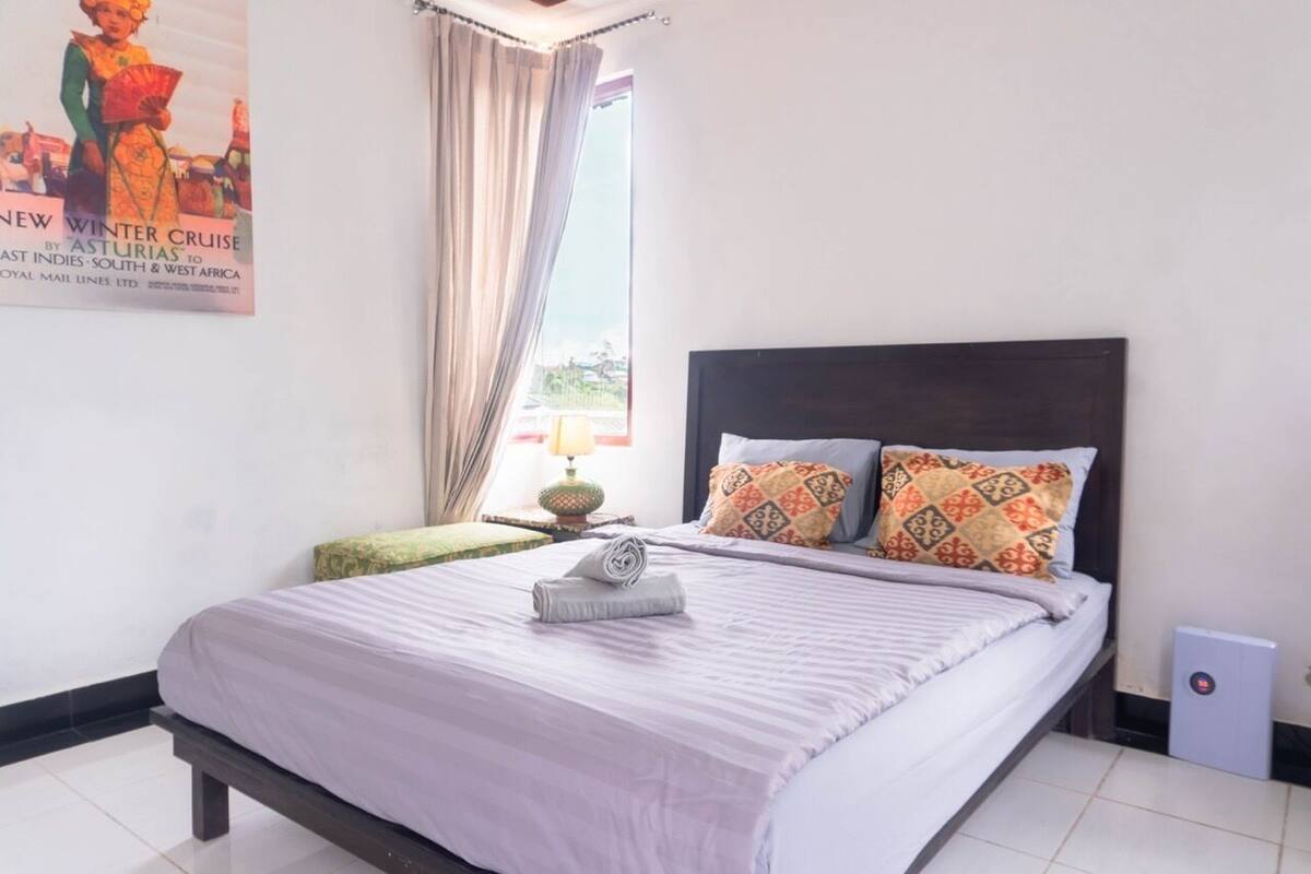 A neatly made bed with a striped bedspread and two patterned pillows, a small nightstand with a lamp, and a poster on the wall.