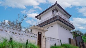 A two-story building with a balcony on the upper floor, surrounded by greenery and a white fence. - Aurora Holiday House Kintamani (Kintamani)
