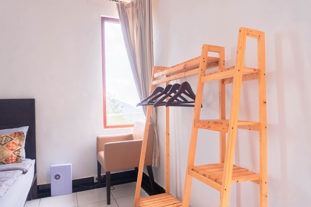 A room with a bed, a chair, a wooden shelf with clothes, and a window with curtains.