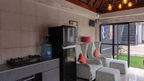 A room with a tiled wall, a black refrigerator, a water dispenser, a gas stove, and a patterned chair with cushions. - Aurora Holiday House Kintamani (Kintamani)