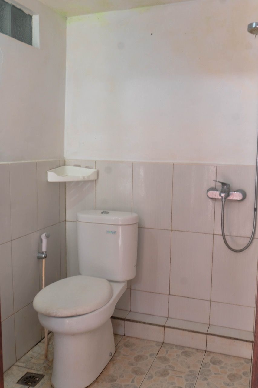 A small, clean bathroom with a toilet, a shower, and a shelf above the toilet.