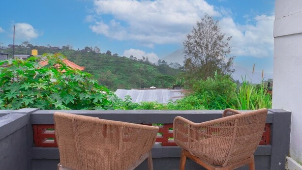Two wicker chairs facing a lush green landscape with a view of a hill and a building with a red roof. - Aurora Holiday House Kintamani (Kintamani)
