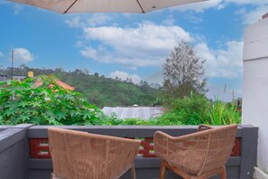 Two wicker chairs facing a lush green landscape with a view of a hill and a building with a red roof. - Aurora Holiday House Kintamani (Kintamani)