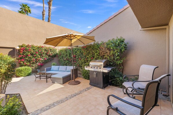 An outdoor patio with a grill, seating, and a pergola.