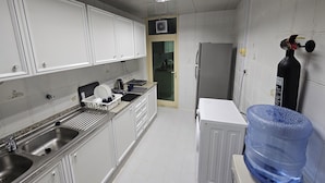 A kitchen with white cabinets, a stainless steel sink, a refrigerator, and a water dispenser. - Oasis Hostel (Abu Dhabi)