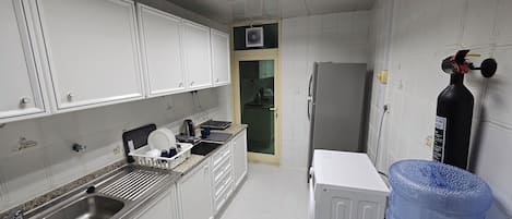 A kitchen with white cabinets, a stainless steel sink, a refrigerator, and a water dispenser.