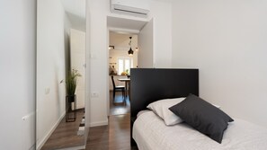 Een slaapkamer met een zwart hoofdeinde, een bed met zwart-witte beddengoed, een potplant en uitzicht op de aangrenzende eetruimte.