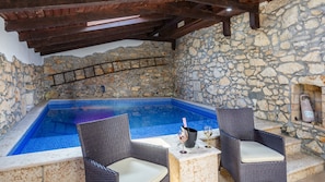 A stone-walled outdoor pool area with a hot tub, wicker chairs, and a stone bench.