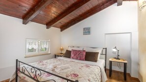 Una camera da letto con soffitto in legno, un letto con biancheria da letto floreale, un comodino con una lampada e una finestra con tende in pizzo.