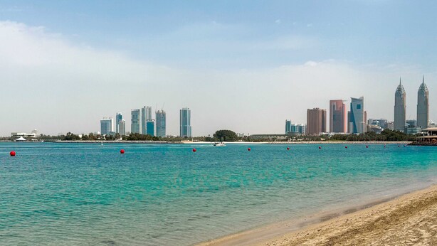 A coastal cityscape with a beach and a skyline of modern high-rise buildings. - LUX The Shoreline Palm Island Suite 2 (Dubai)