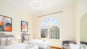 A hotel room with two beds, a large arched window with a city view, and abstract art on the walls. - LUX The Shoreline Palm Island Suite 2 (Dubai)