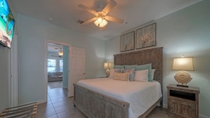 A bedroom with a wooden bed, two bedside lamps, a ceiling fan, and a small wooden nightstand with a decorative item.