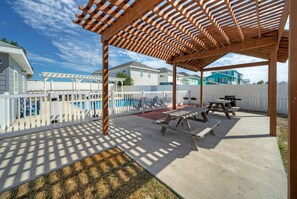A covered outdoor patio with picnic tables and a pool in the background. - Sleeps 16 w/ Pool + Minutes to Beach | Costa Bahia - 2 Condos (Port Aransas)