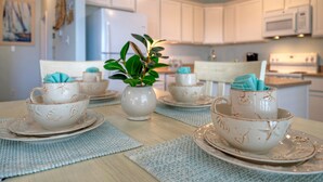 A kitchen with white cabinets, a microwave, and a stove. There are two white cups with blue napkins on the table.