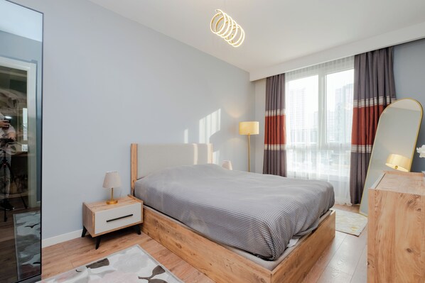 A modern bedroom with a wooden bed, bedside tables, a mirror, and a city view through large windows. - lUX Residence on High Floor 03 (Istanbul)