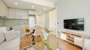 Una sala de estar moderna con una mesa de centro de vidrio, un sofá, un televisor y una cocina al fondo.
