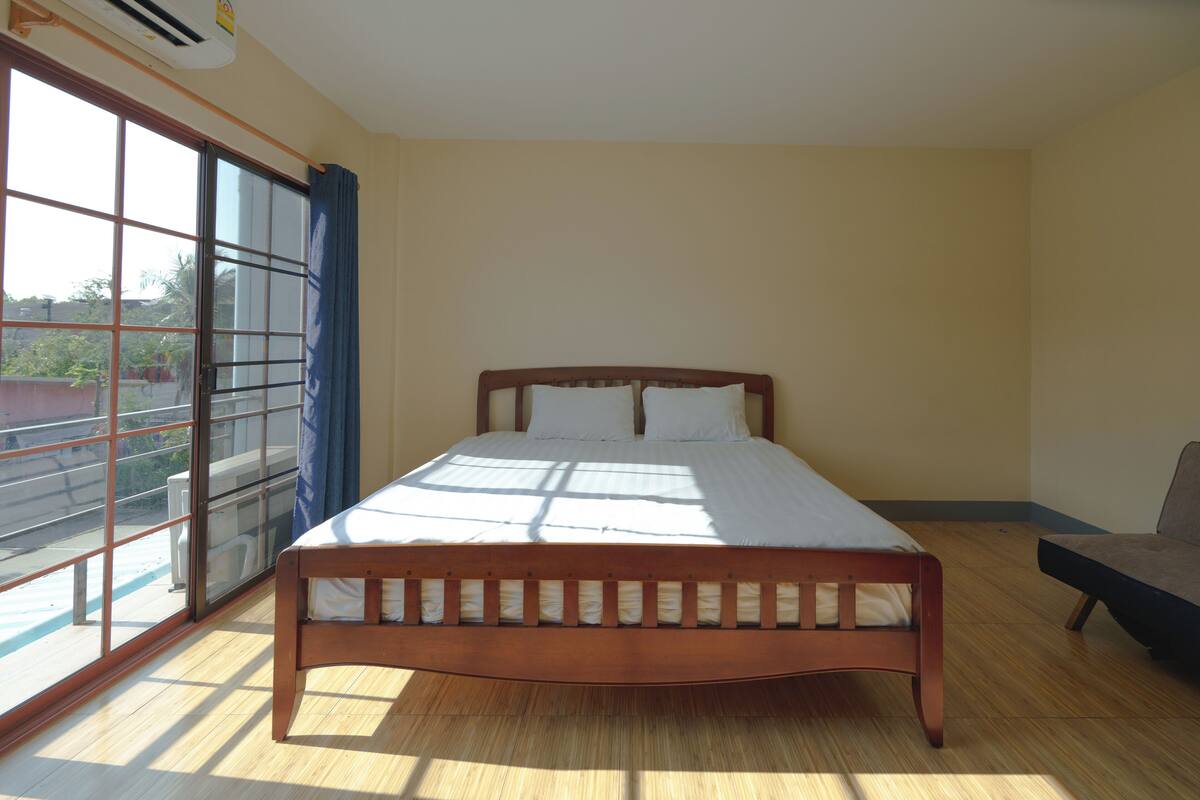 A bedroom with a wooden bed, a large window with curtains, and a view of the outside.