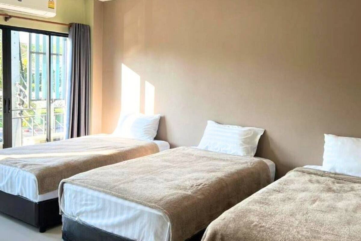 A hotel room with two beds, a large window with curtains, and a view of greenery outside.