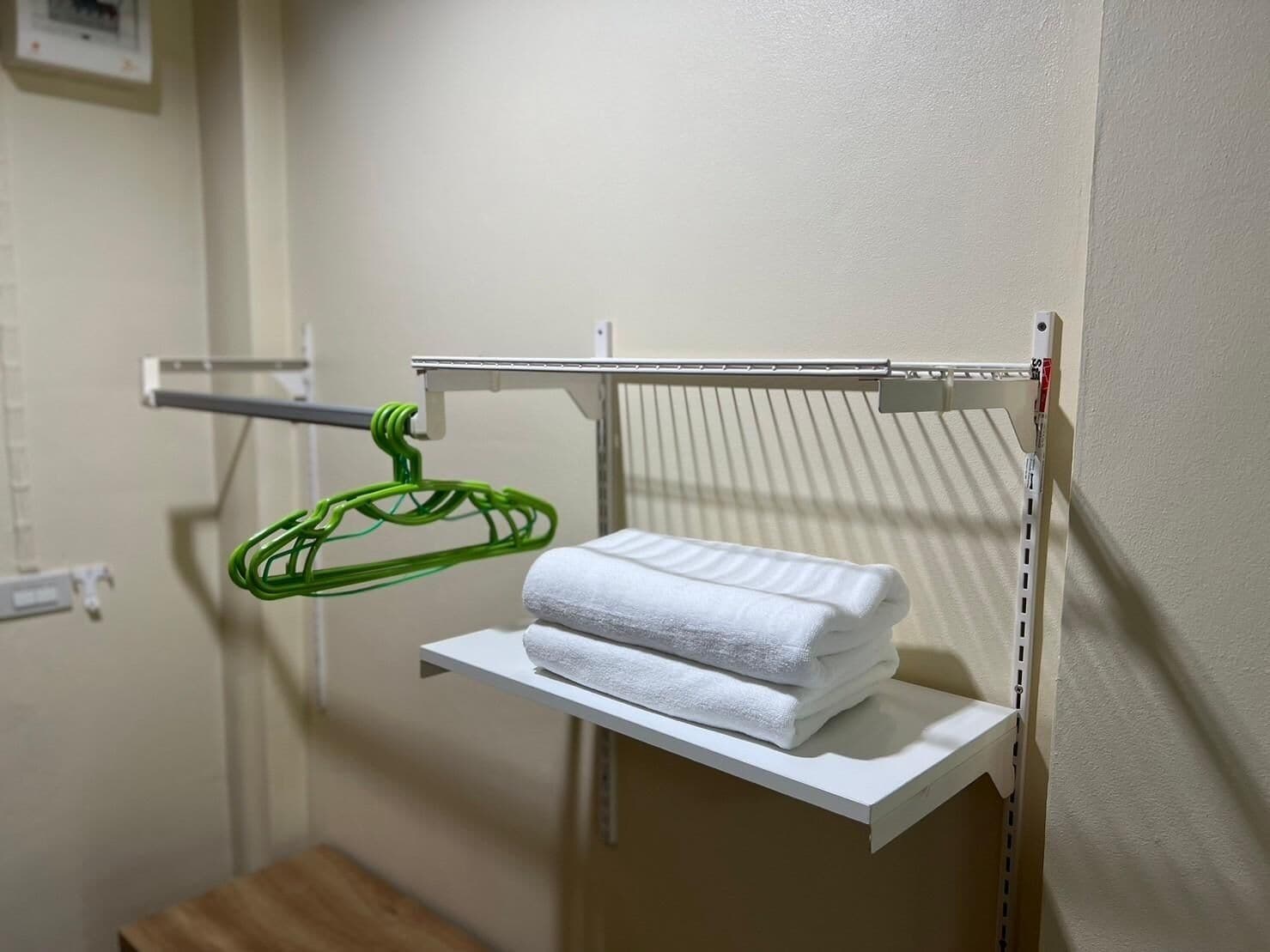 A bathroom with a towel rack holding a green hanger and a stack of white towels on a shelf.