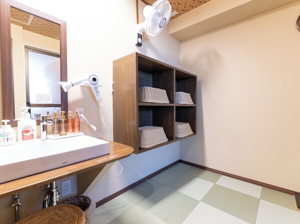 A bathroom with a wooden vanity, a mirror, a hairdryer, and shelves with folded towels. - Hotel Boujosou (Kazuno)