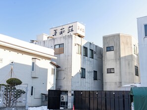 A modern building with a sign in Japanese, a gated entrance, and a snow-covered ground. - Hotel Boujosou (Kazuno)