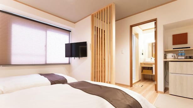 A modern hotel room with two beds, a TV mounted on the wall, and a kitchenette area. - Hotel Boujosou (Kazuno)