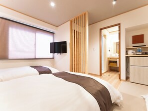 Habitació d'hotel moderna amb dos llits, una televisió penjada a la pared i una zona de cuina.
