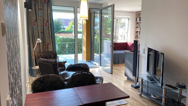 A modern living room with a dining area, a sofa, a TV, and a glass door leading to a balcony. - Ketzin Havel modern apartment with private garden, close to the water (ketzin)