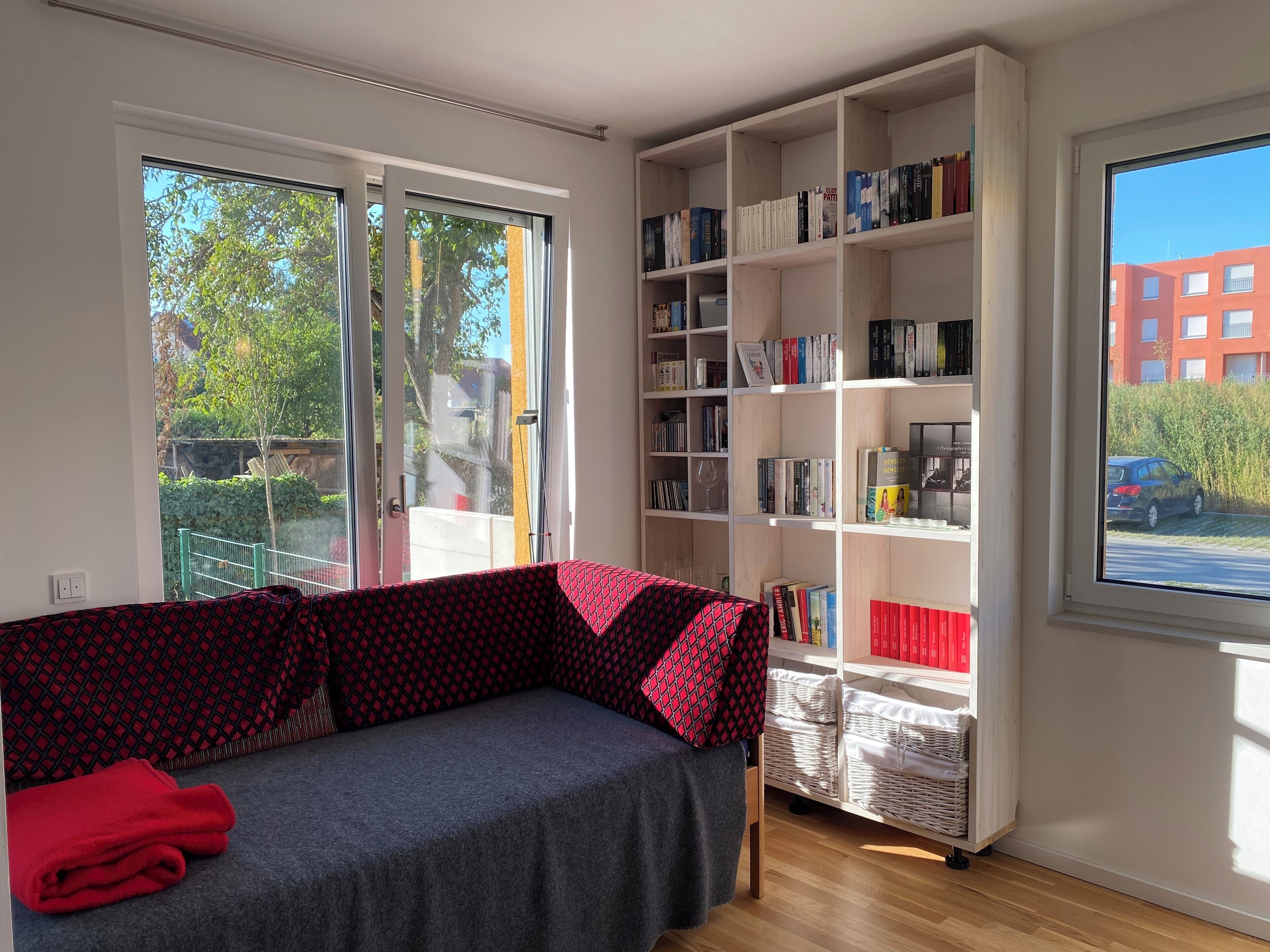 Una habitación con un sofá, una estantería y una ventana que da a un edificio y un coche.