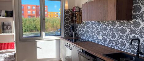 A modern kitchen with a large window, wooden cabinets, and a built-in dishwasher.