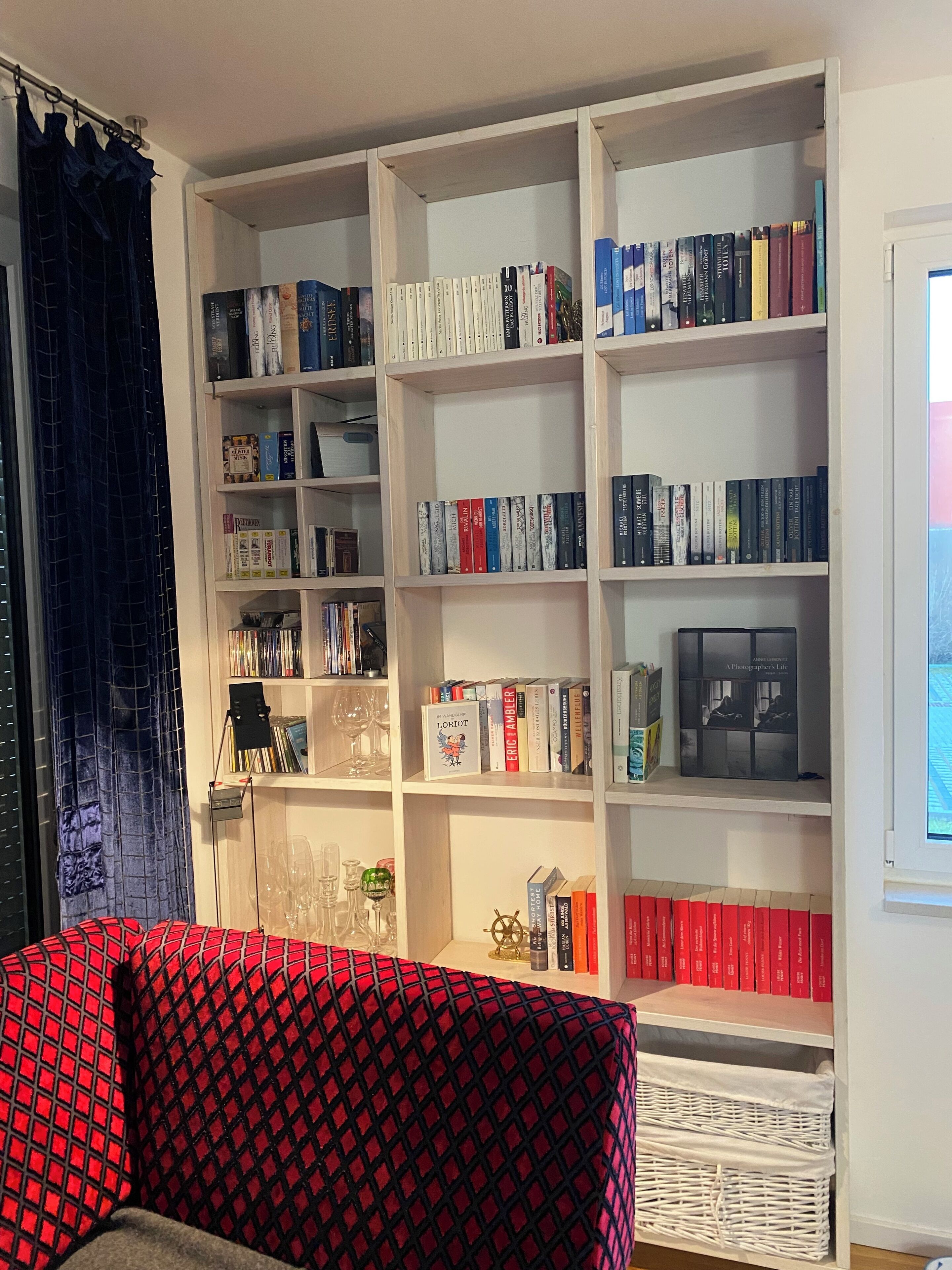 Een kamer met een grote boekenkast vol boeken, een rode gestreept bank en een raam met gordijnen.